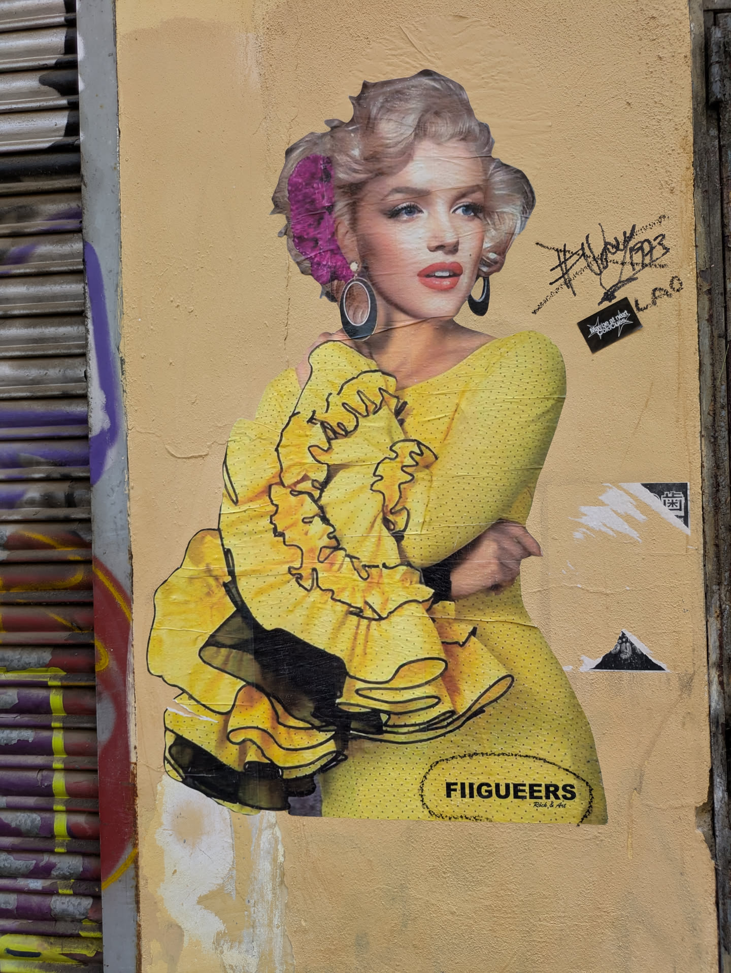 This is a sticker featuring a modified image of Marilyn Monroe wearing a yellow dress with ruffles and a purple flower in her hair. The sticker is on a yellow wall. At the bottom, there's the text "FIIGUEERS" followed by "Rich & Art". Above the sticker, there are a few signatures and other small stickers.