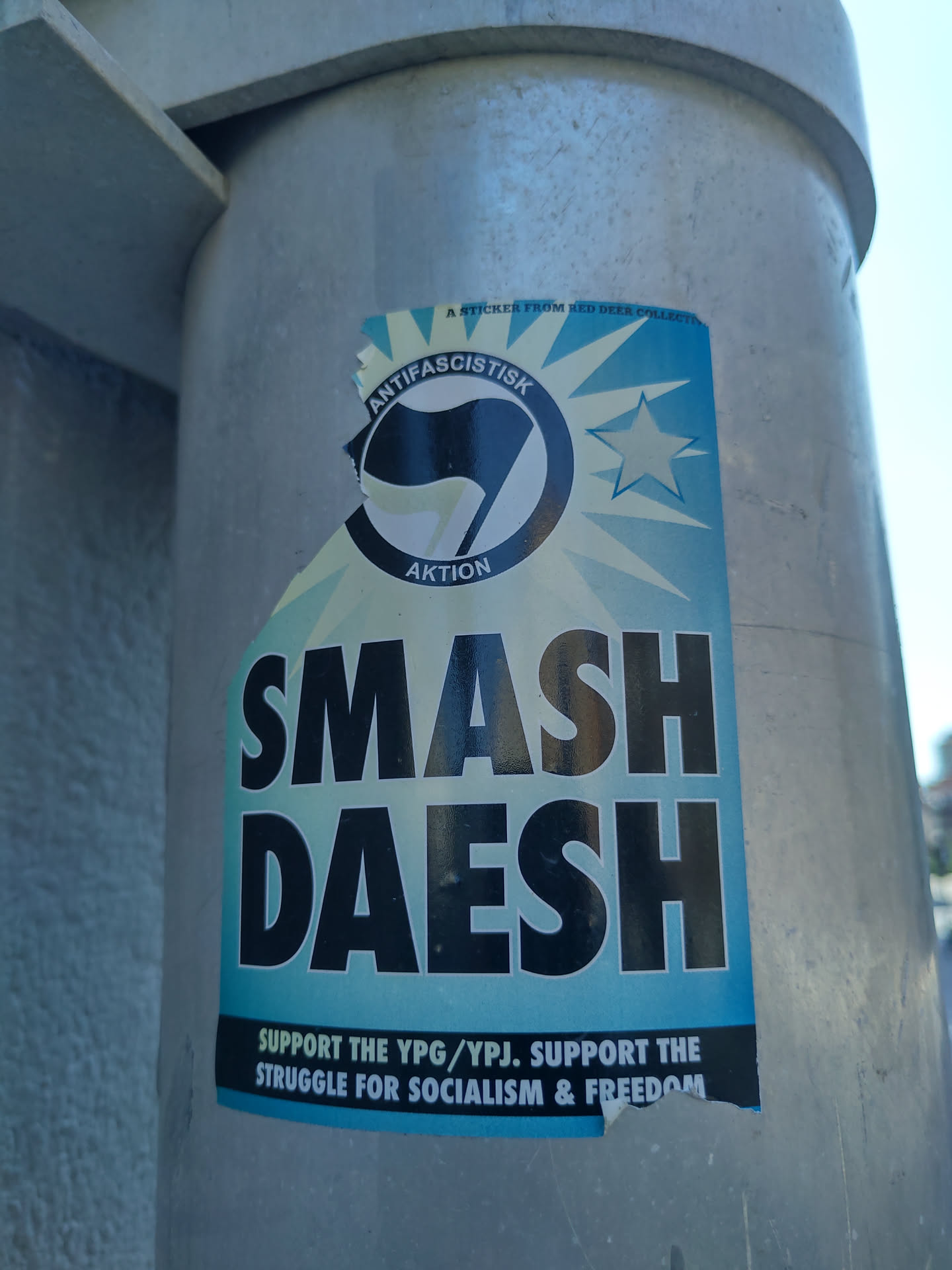 A sticker promoting the YPG/YPJ and advocating for socialism and freedom. The sticker features the antifascist symbol and the slogan "Smash Daesh."