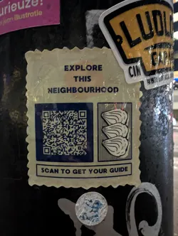 A sticker with a QR code inviting people to scan it to get a neighbourhood guide. The sticker also features an illustration of three scallops or similar shellfish.