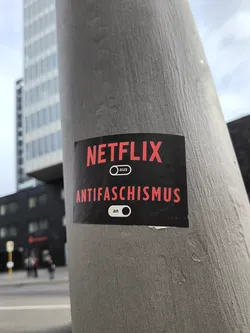 A sticker on a pole with the Netflix logo and the word Antifaschismus with an on/off switch indicating it's on. The words "aus" (off) and "an" (on) are written next to the switch.