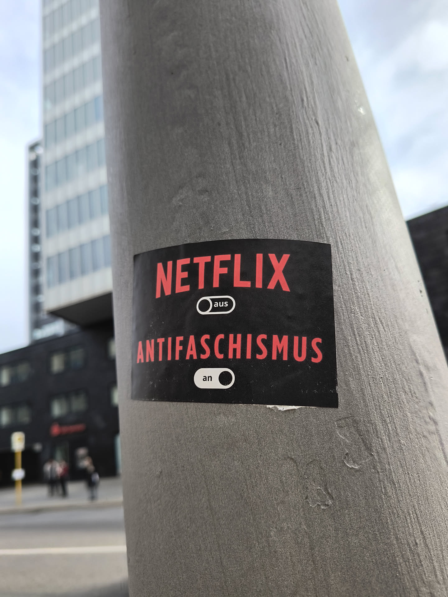 A sticker on a pole with the Netflix logo and the word Antifaschismus with an on/off switch indicating it's on. The words "aus" (off) and "an" (on) are written next to the switch.