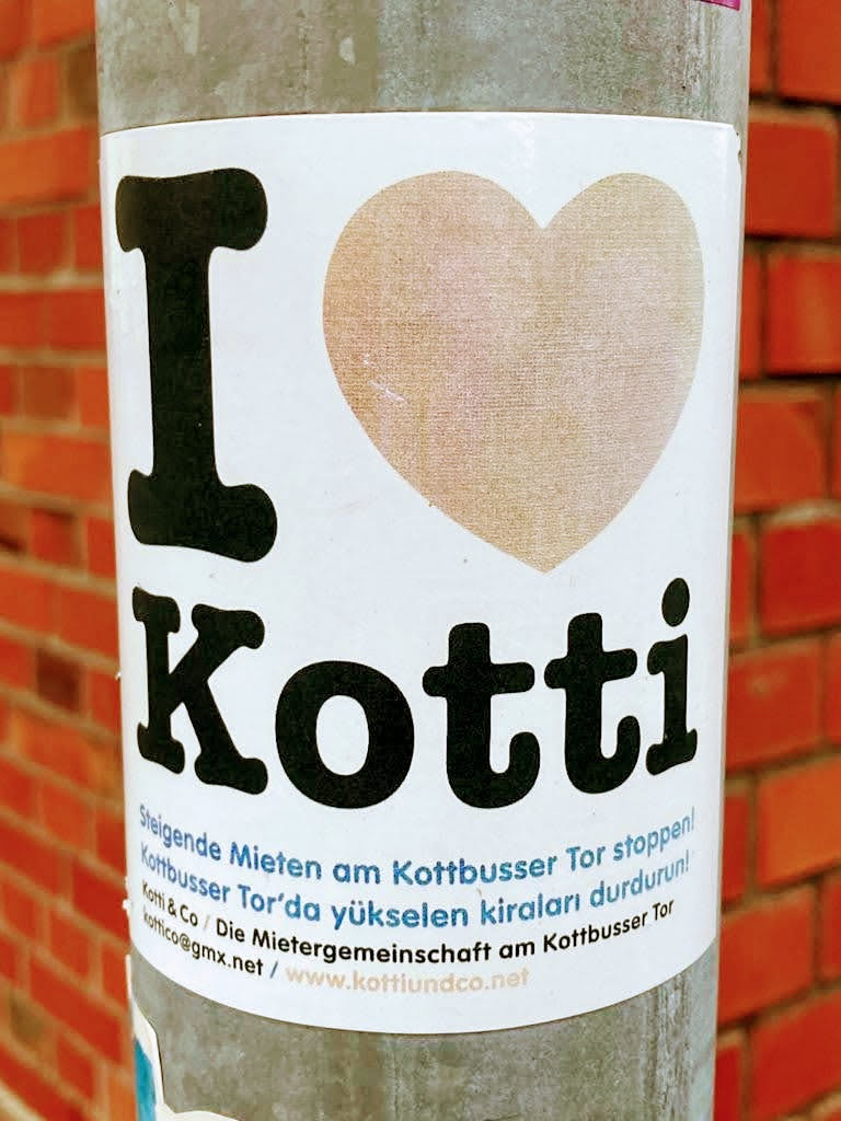 Sticker expressing love for the Kottbusser Tor neighborhood in Berlin and advocating against rising rents.  It features a heart design and contact information for a tenant community.