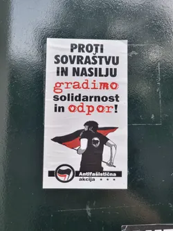 A sticker with an illustration of a person holding a black and red flag. The text on the sticker is in Slovenian and translates to "Against hatred and violence, we build solidarity and resistance!"