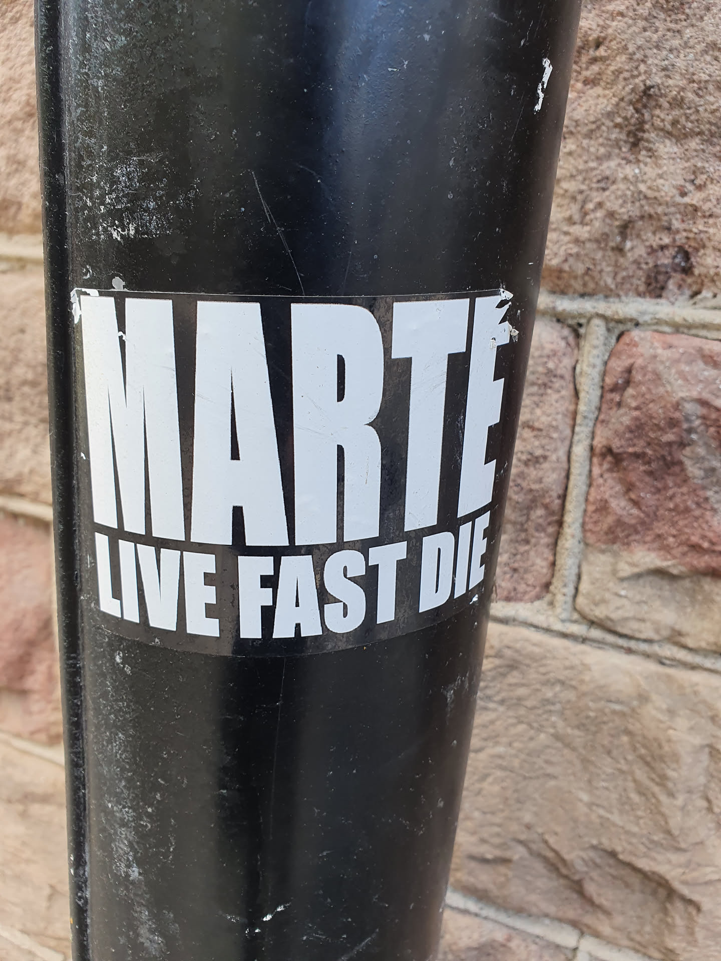 A black and white sticker with the word MARTE and the phrase LIVE FAST DIE. The sticker is applied to a black cylindrical object.