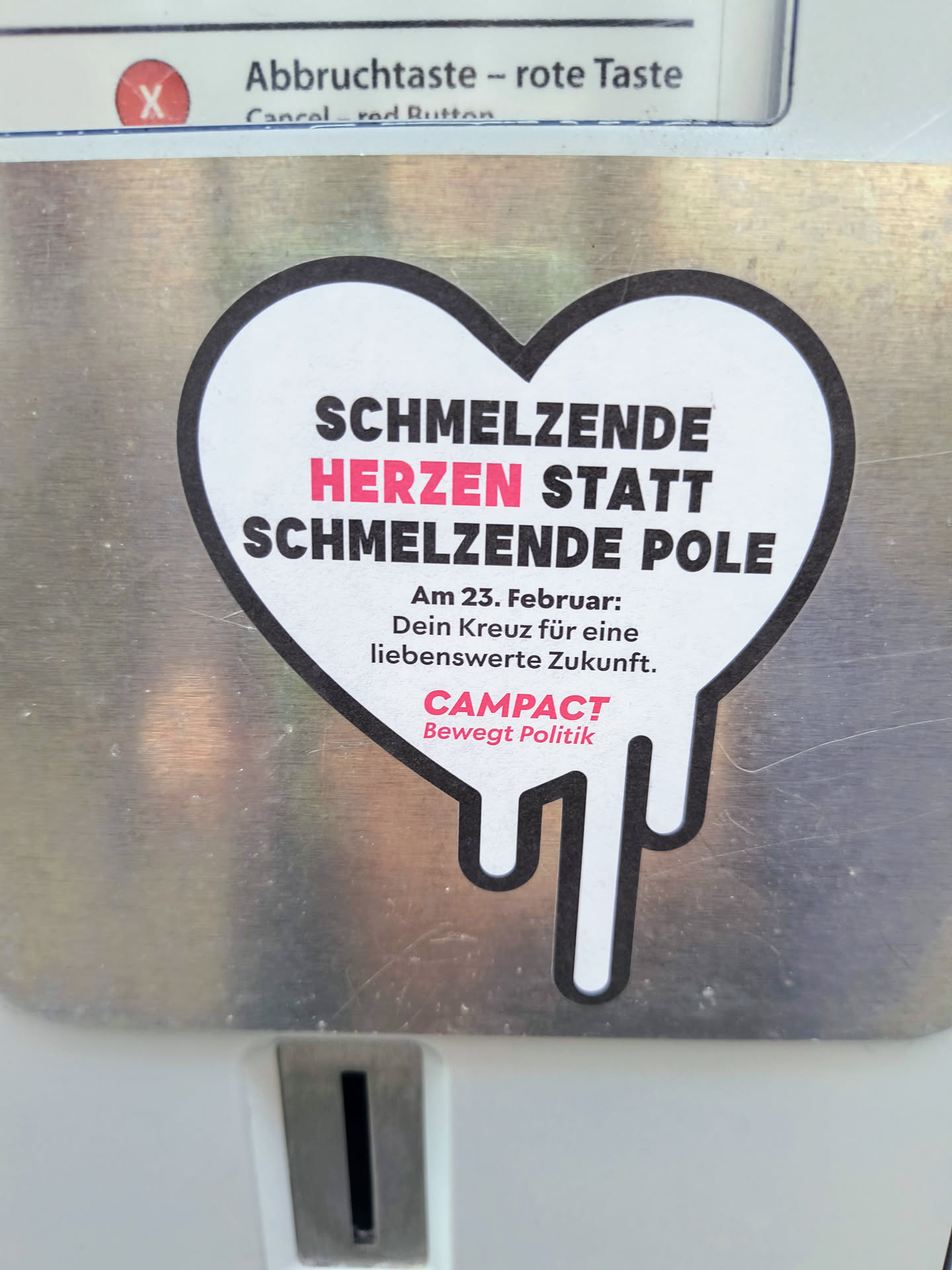 The sticker is heart-shaped with black and white colors, except for the word 'Herzen' which is in pink. The heart shape is slightly melted at the bottom. The text on the sticker says, 'Schmelzende Herzen statt schmelzende Pole. Am 23. Februar: Dein Kreuz für eine liebenswerte Zukunft.' at the top, and 'Campact. Bewegt Politik' at the bottom.