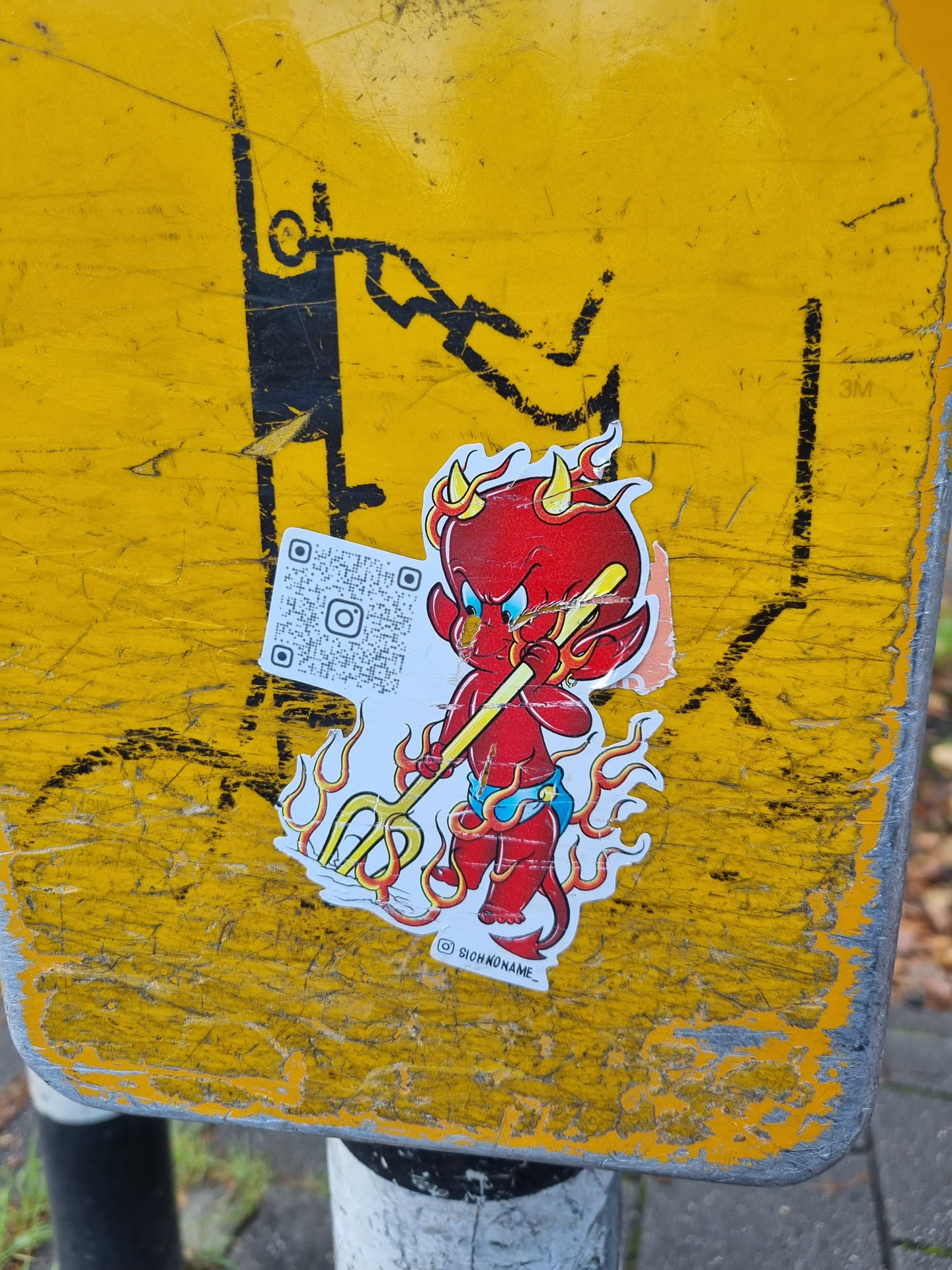 A sticker featuring a cartoon devil with flames, holding a pitchfork. The sticker has a QR code and the artist's signature. 