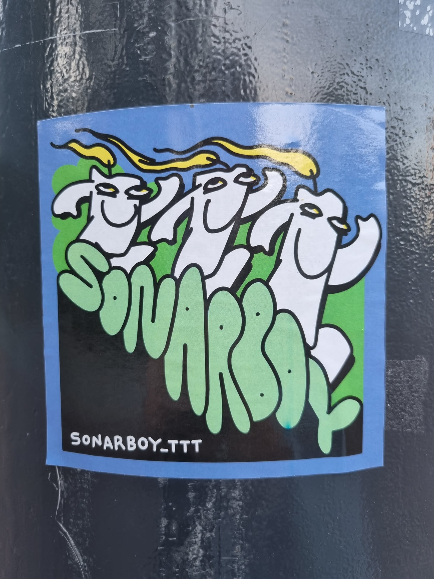 A sticker featuring three stylized figures with flame-like hair, set against a backdrop of green hills and a blue sky. The text 'SONARBOY_TTT' is visible at the bottom.  The art style is playful and cartoonish.