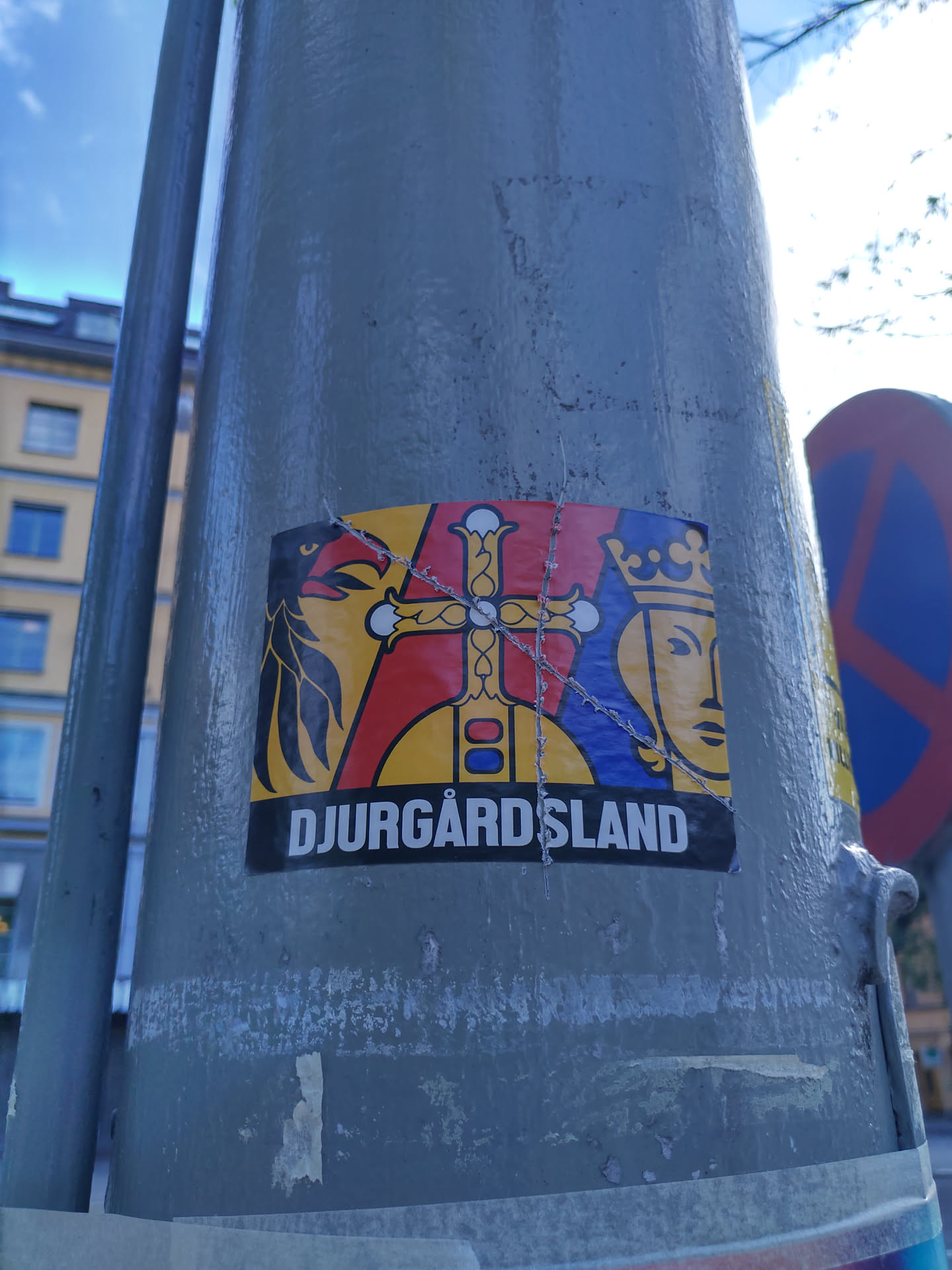 A sticker featuring a stylized coat of arms with a bird, cross, and crowned figure. The text 'DJURGÅRDSLAND' is visible at the bottom.