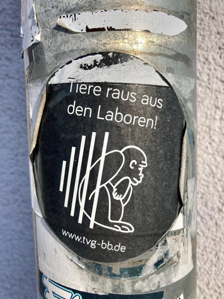 A black and white sticker with a design depicting an ape sitting behind bars. The text on the sticker says 'Animals out of the labs!' in German and includes a website address.