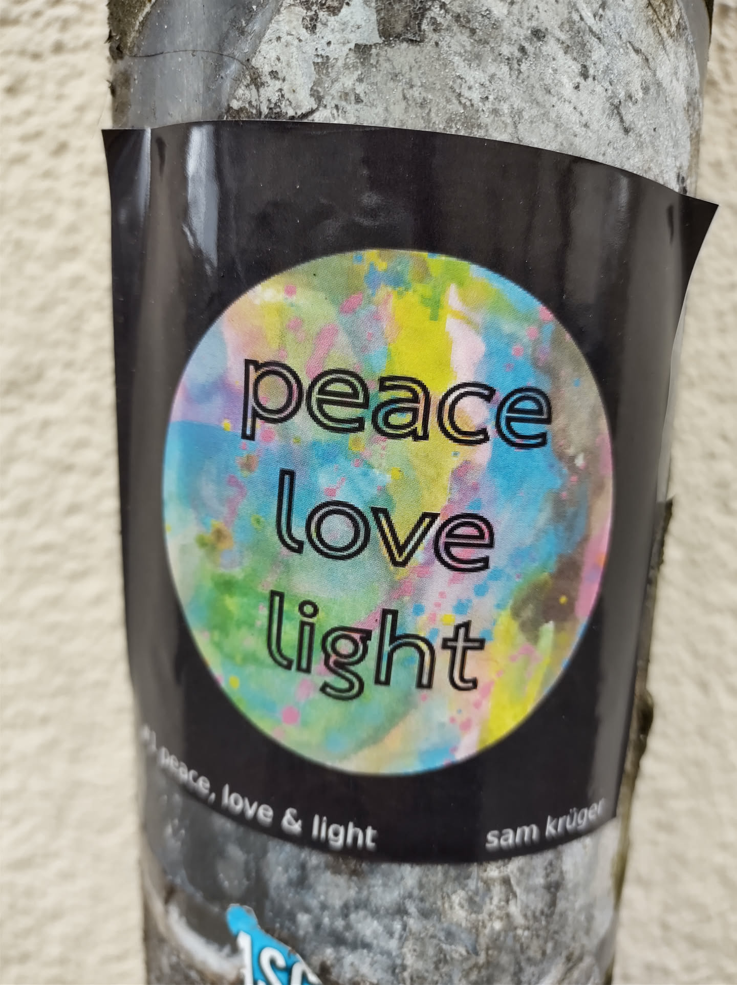 Round sticker on a dark background with a colorful paint splatter design. The words "peace love light" are written in a stylized font.