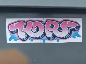 A sticker with pink and blue graffiti-style lettering that says "YORS." The sticker has a distressed look, with cracks in the surface. There is a small "17" visible within the lettering.