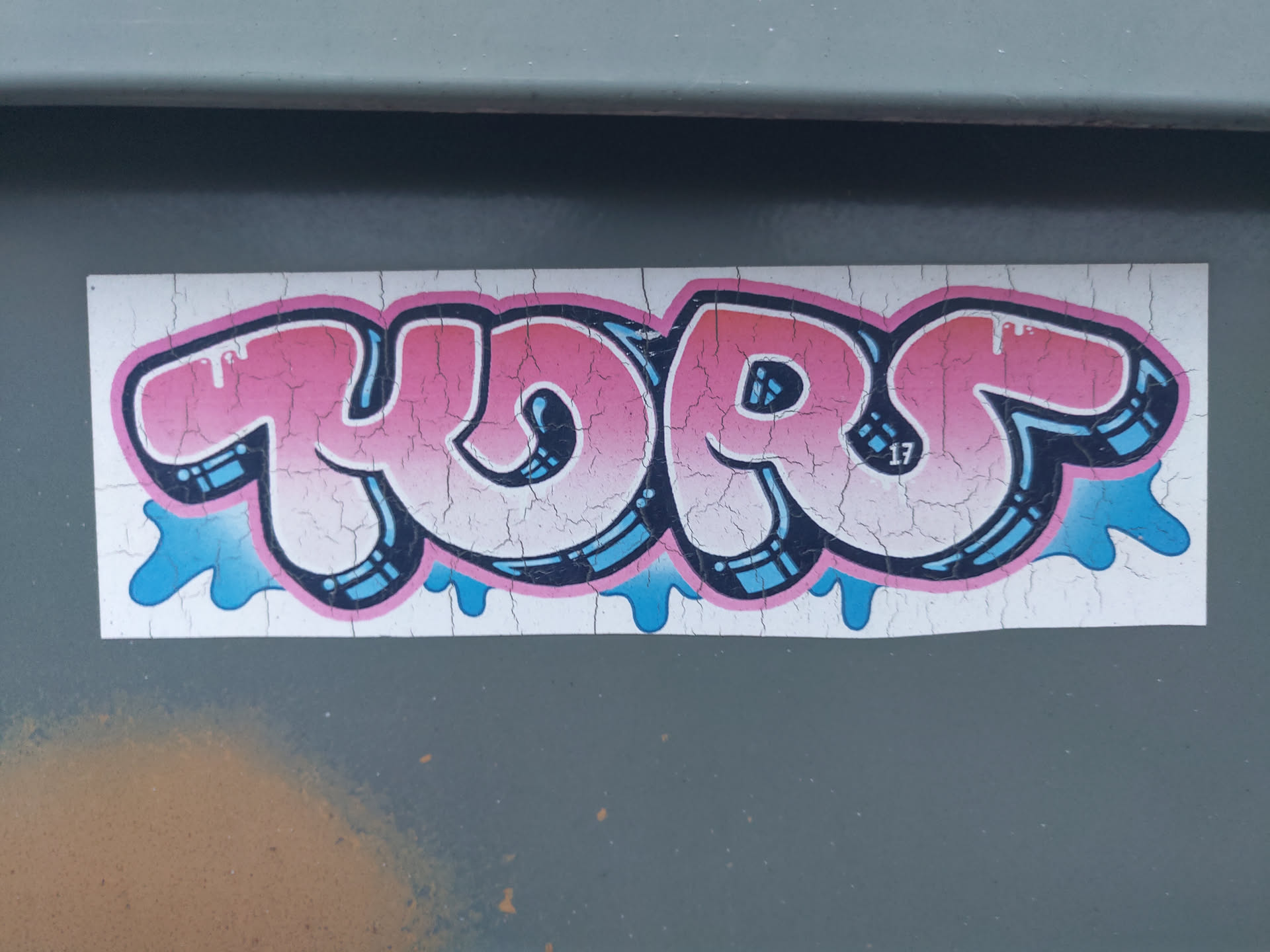 A sticker with pink and blue graffiti-style lettering that says "YORS." The sticker has a distressed look, with cracks in the surface. There is a small "17" visible within the lettering.