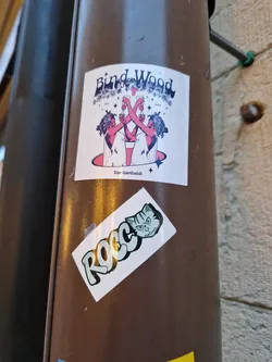A sticker featuring an illustration of two women toasting with wine glasses, with the text 'Bind Wood' and 'Bar Garibaldi'. Another sticker featuring a stylized cat illustration with the name Rocco is placed below the first one.
