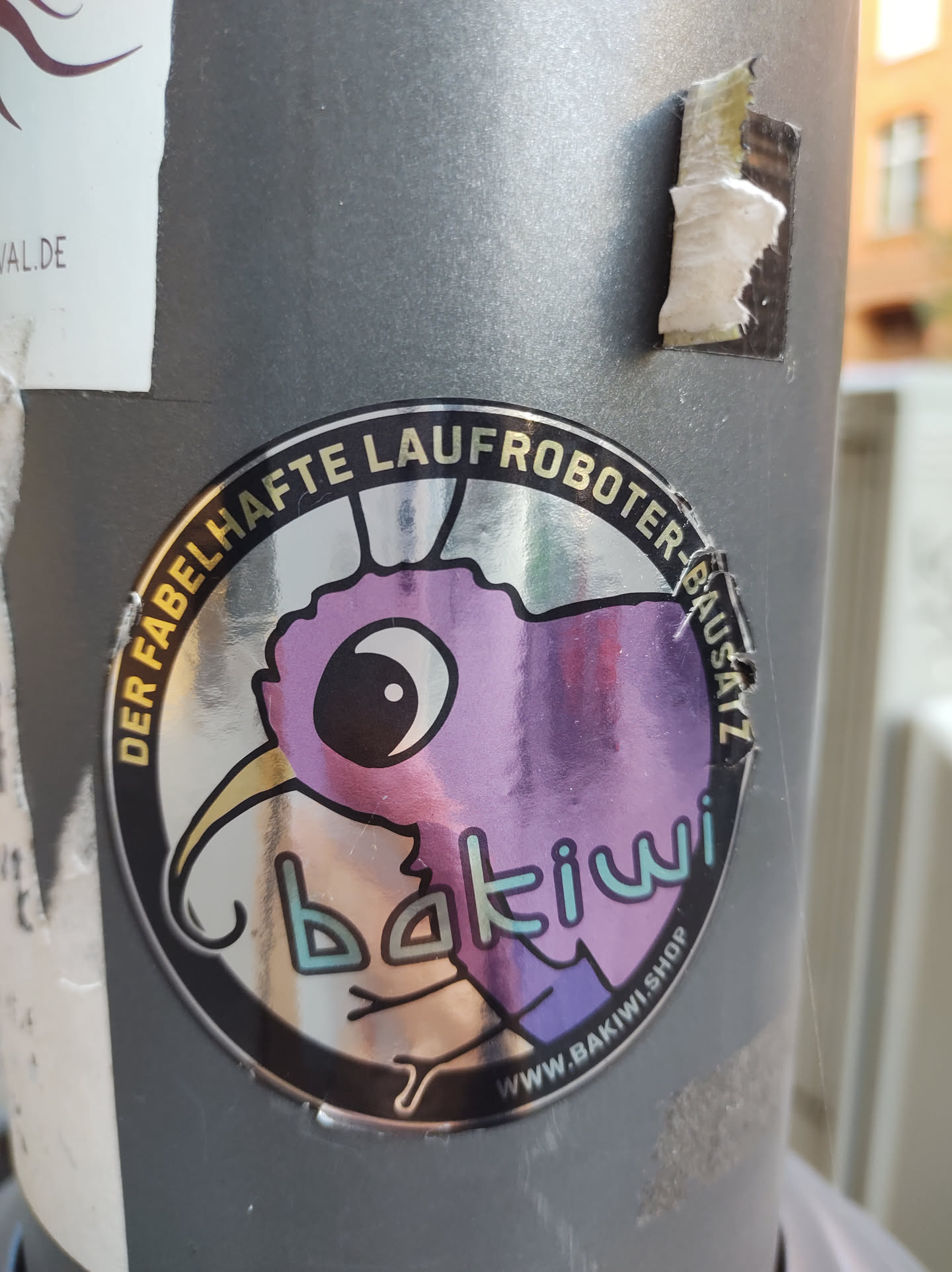 A round sticker featuring a whimsical purple creature, possibly a bird or kiwi, with the text "bakkiwi" prominently displayed.  The surrounding text in German translates to  "The fabulous Laufroboter Bausatz" which could refer to a kit or product.  The sticker also includes a website address.