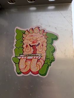 This sticker features a unique character design with a vibrant color palette, seemingly enjoying a meal. The art style is hand-drawn, with a mix of graphic elements. 