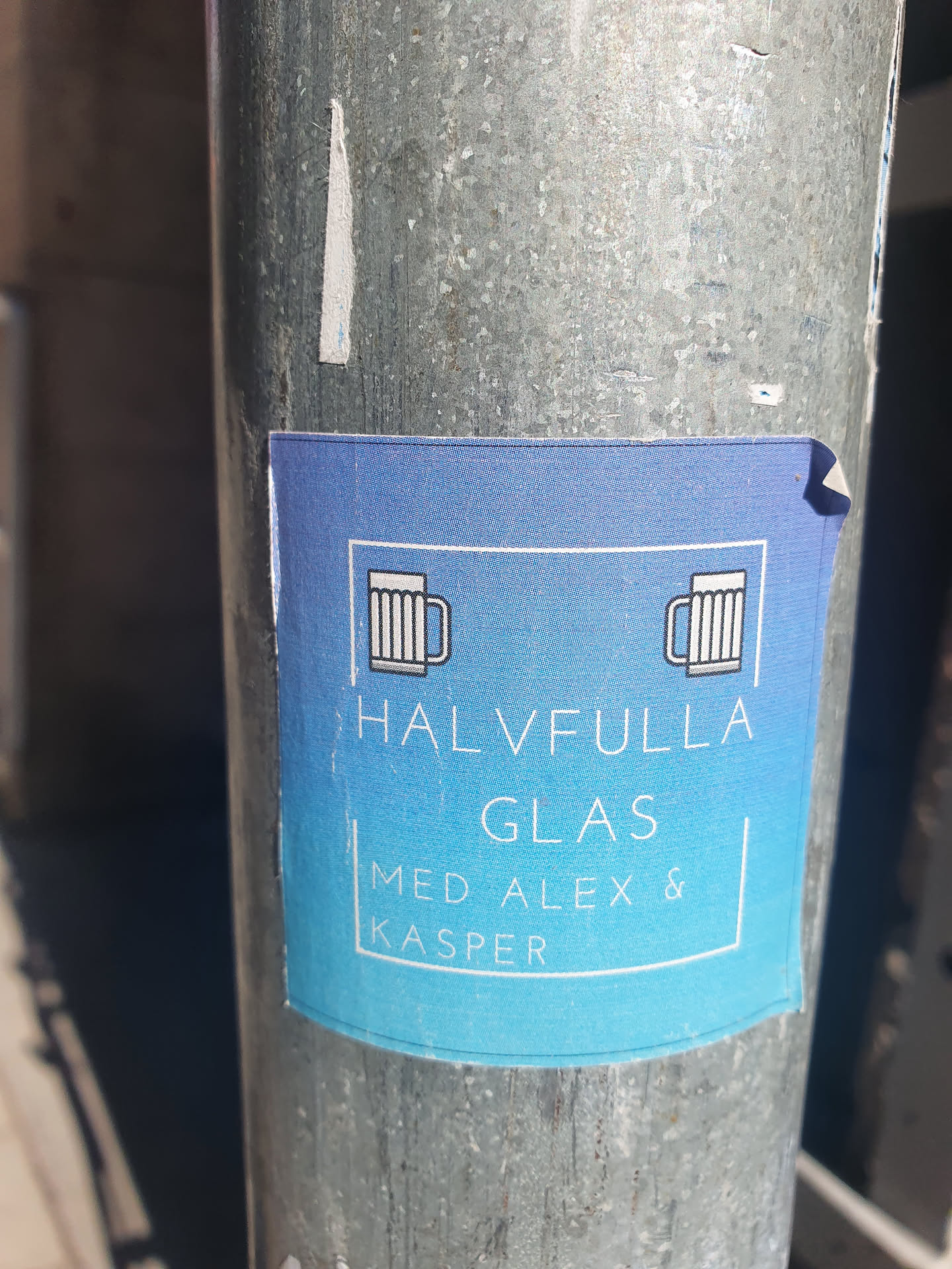 A blue sticker with a simple design featuring two beer mugs and the text 'HALVFULLA GLAS MED ALEX & KASPER'.