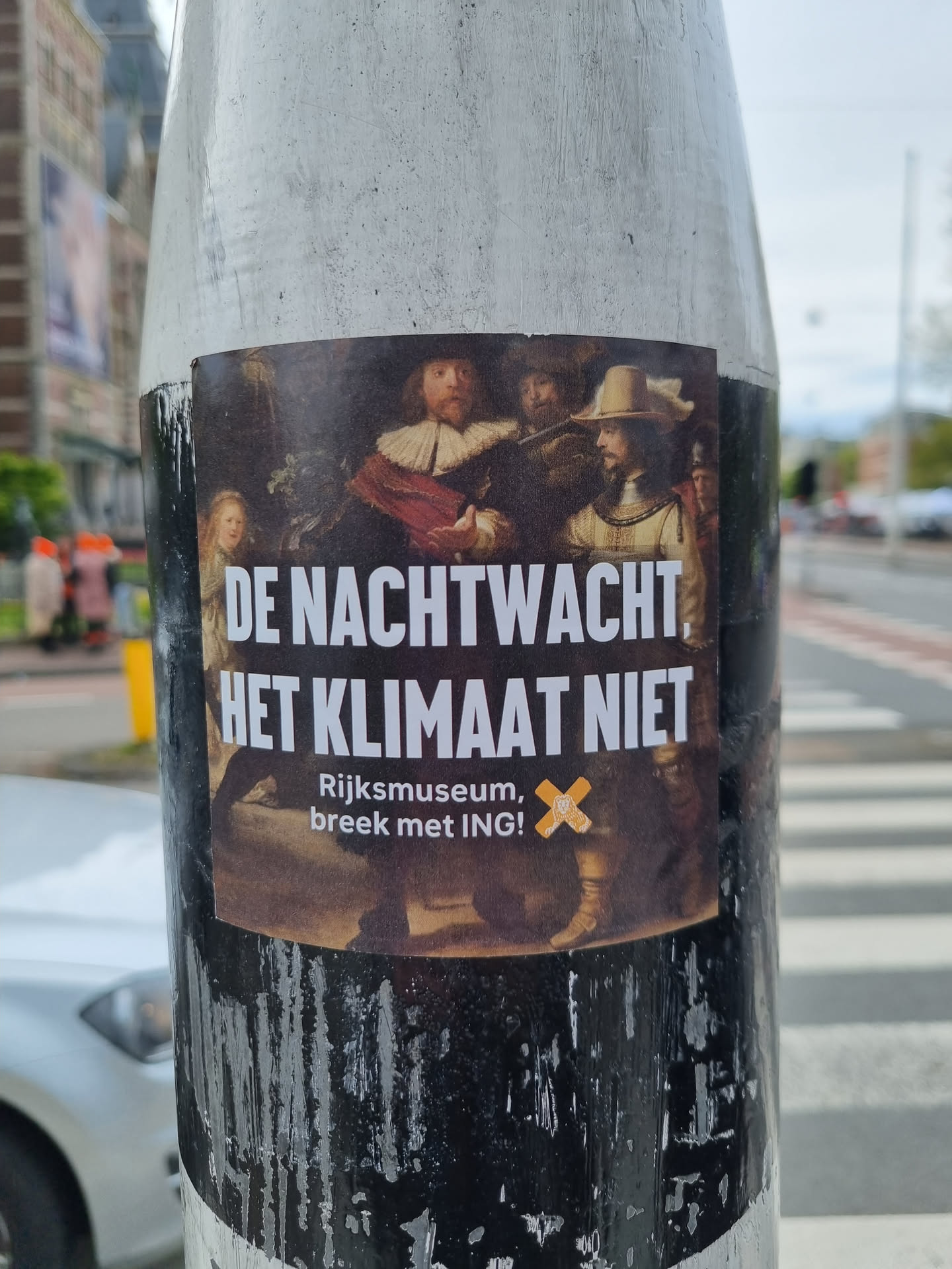 A sticker featuring a detail of Rembrandt's 'The Night Watch' with text overlay in Dutch.  The text translates to: 'The Night Watch, not the climate. Rijksmuseum, break with ING!' It appears to be a protest or activism sticker.