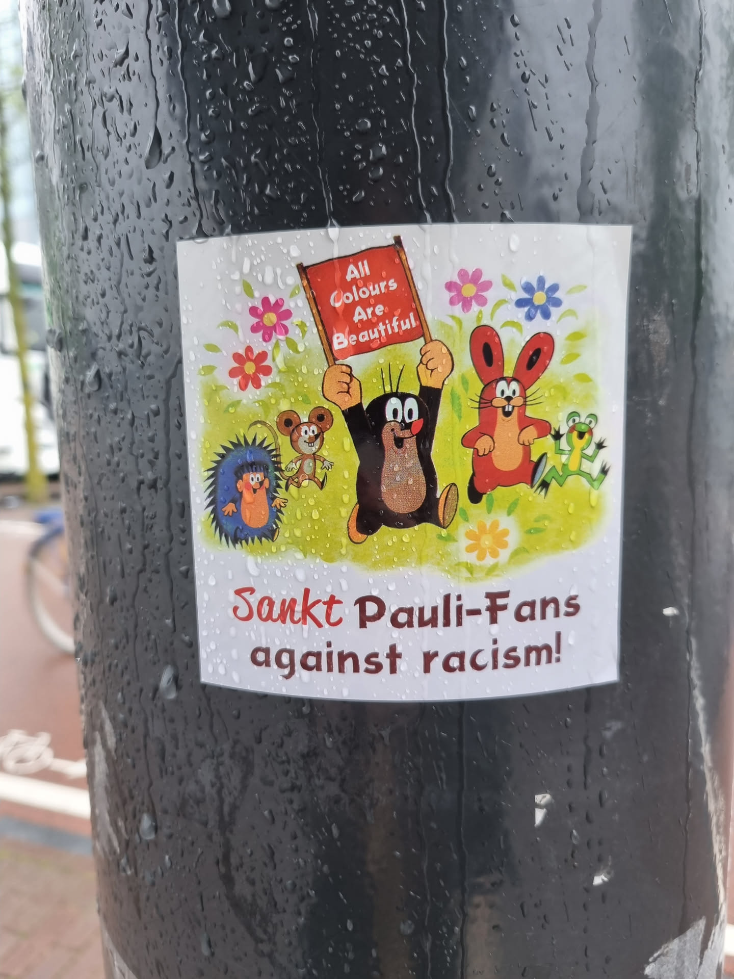 A sticker featuring Krtek (Mole) and friends, holding a banner that says "All Colours Are Beautiful."  The sticker also displays the text: "St. Pauli-Fans against racism!"
