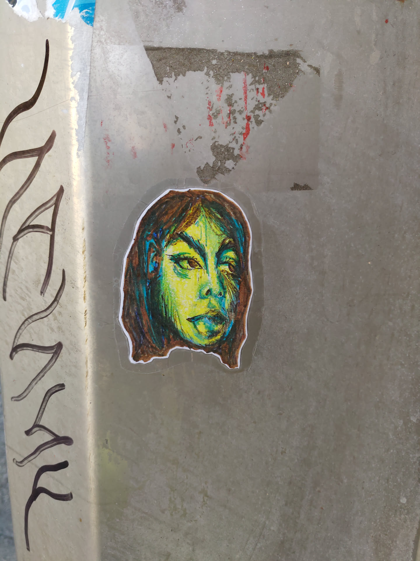 A sticker of a stylized female face with green and yellow tones. The style is reminiscent of a sketch or drawing, with visible lines and shading.