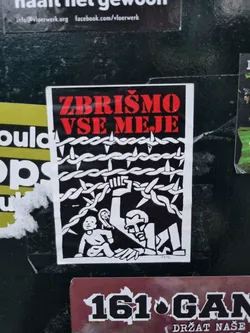 A black and white sticker with red text. The text in the sticker says "Zbrišimo vse meje", which translates to "Let's erase all borders". The image depicts a person reaching over a barbed wire fence to help a child. 