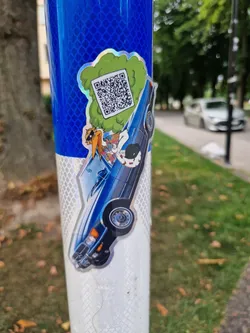 A vibrant sticker featuring Daffy Duck in a classic blue car. A QR code is prominently displayed within a green cloud behind the car. The sticker has a glossy, holographic effect. 