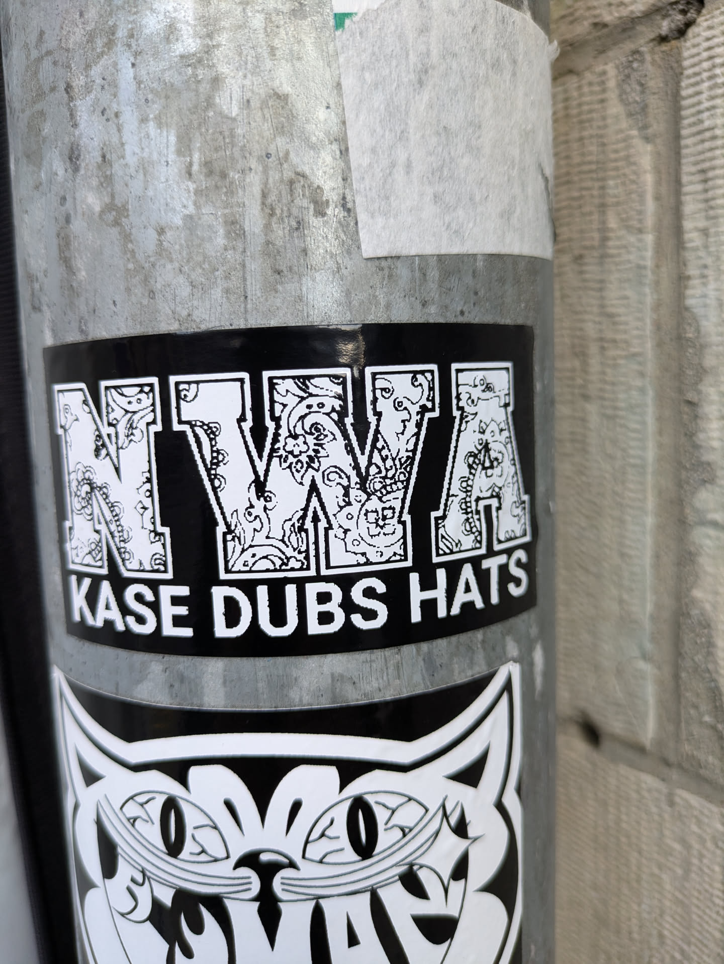 Black and white sticker with the letters NWA in a stylized font, with a paisley-like pattern inside each letter. Below the letters is the text "Kase Dubs Hats".