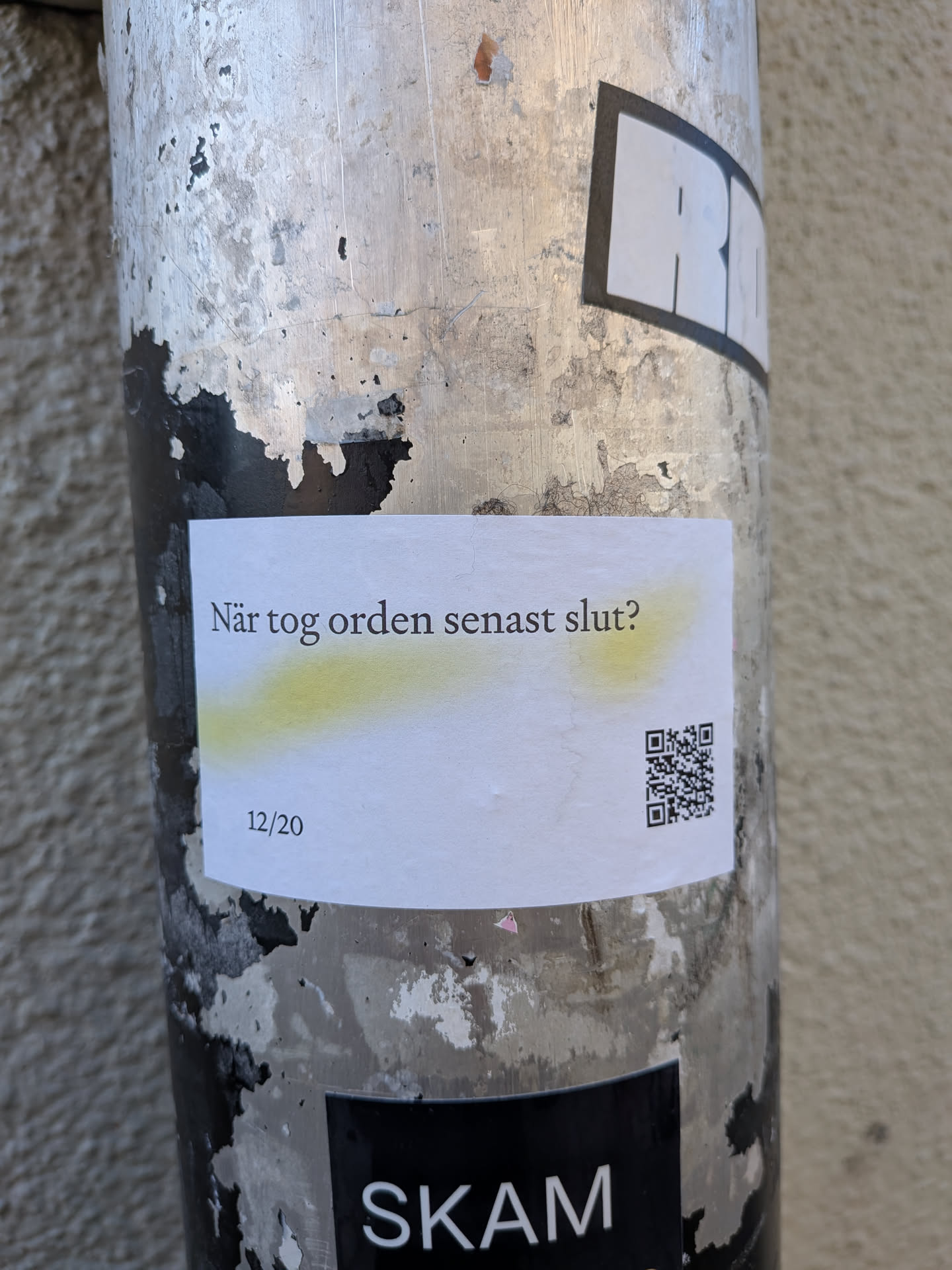 A rectangular white sticker adhered to a weathered, metallic pole. The sticker features the Swedish text "När tog orden senast slut?" (When did the words last run out?) in a dark grey, sans-serif font, with a subtle yellow highlight underneath. In the bottom left corner, the date "12/20" is printed, and in the bottom right corner, there is a black and white QR code. The sticker appears slightly creased and worn, indicating its physical presence in an urban environment.