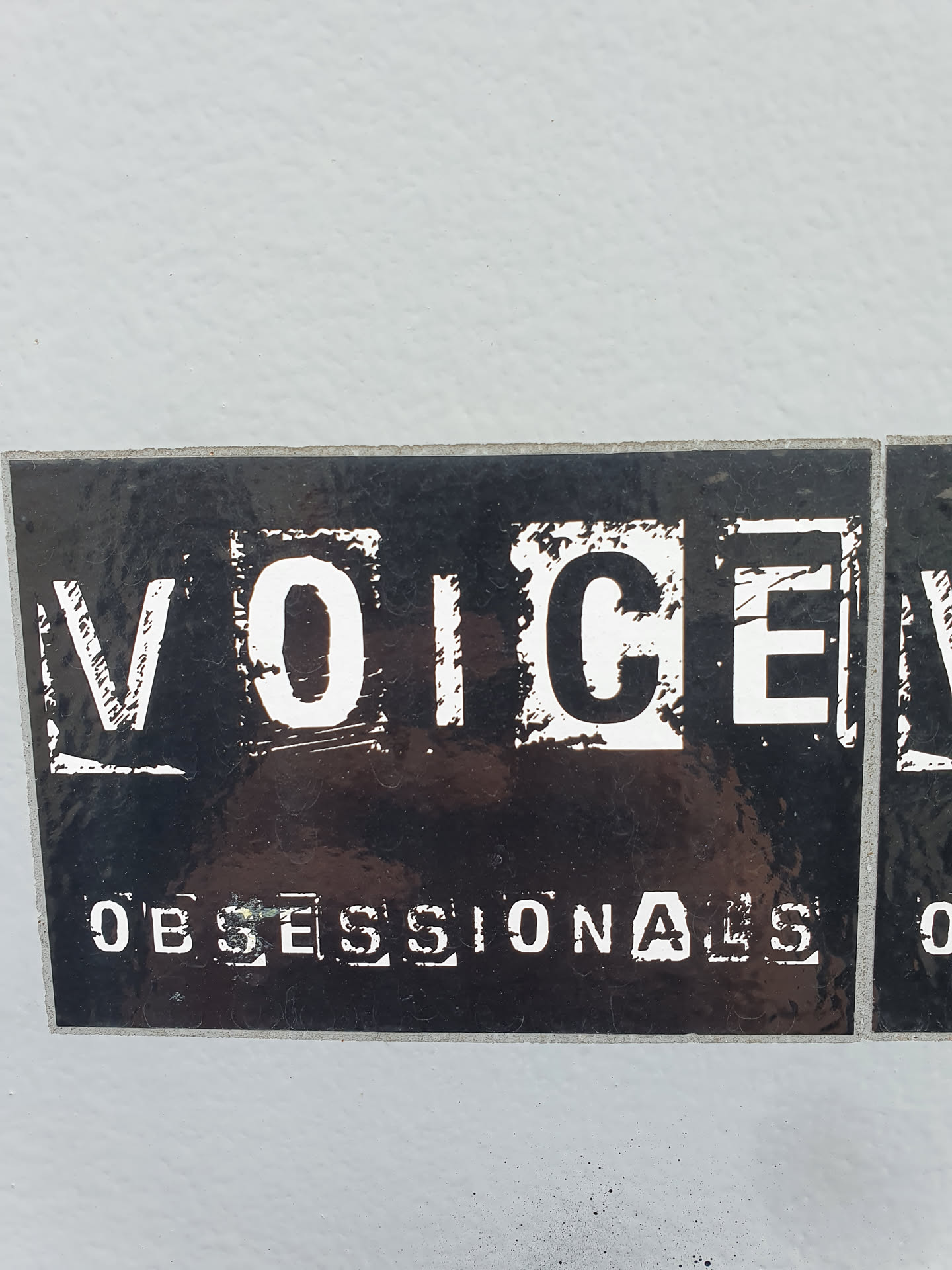 Black and white sticker with the text "VOICE" in a bold, blocky font, and below it, "OBSESSIONALS" in a similar style. The sticker has a slightly distressed or grunge aesthetic.