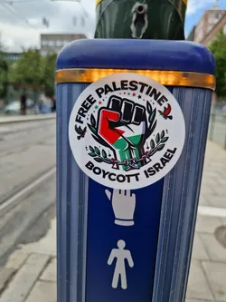 A sticker expressing support for Palestine and calling for a boycott of Israel. It features a fist with the Palestinian flag colors, olive branches, and the words "Free Palestine" and "Boycott Israel".