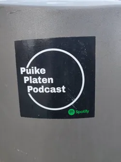Black and white sticker with the text "Puikie Platen Podcast" in a circle.  Spotify logo is present at the bottom.