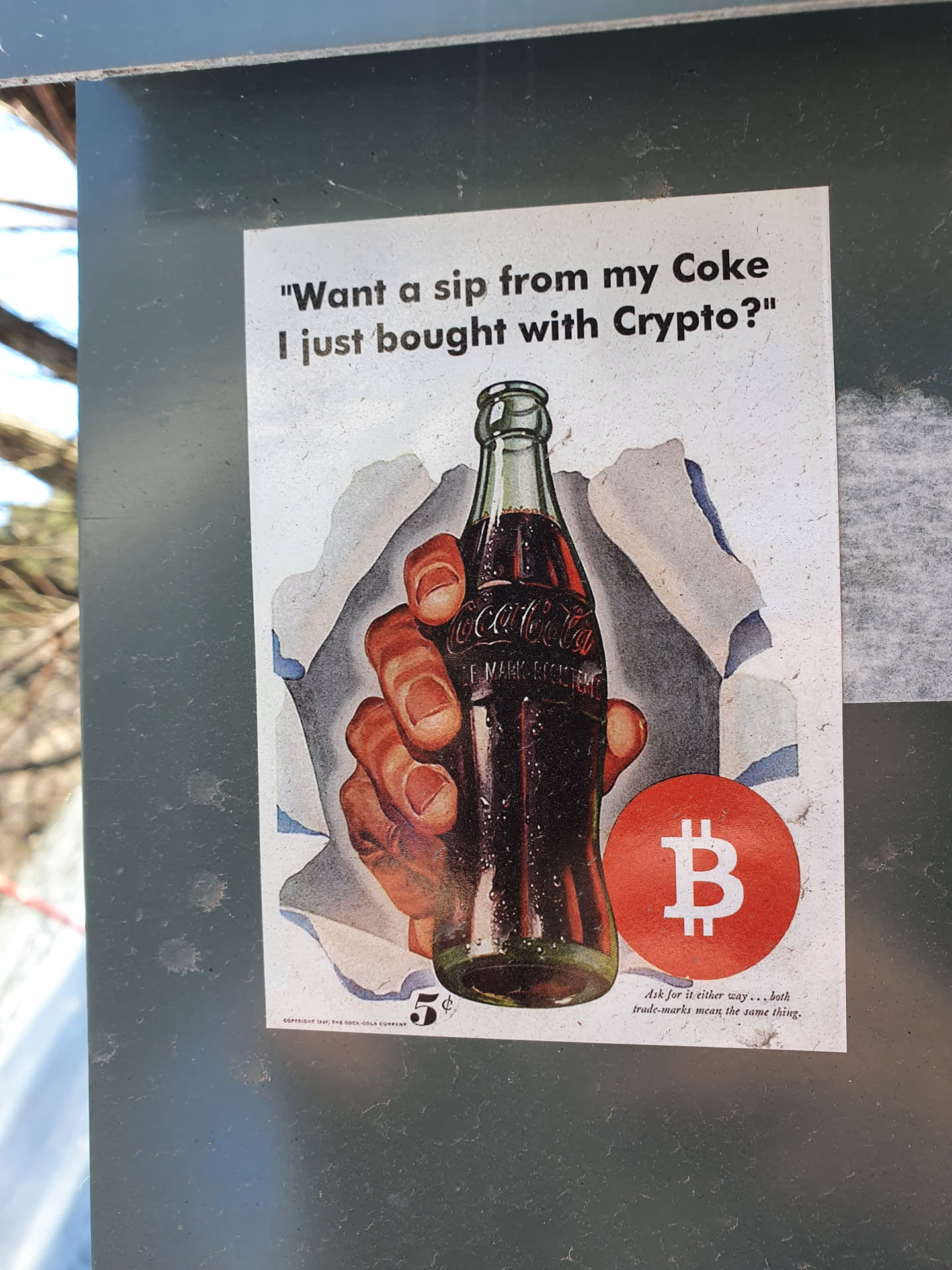 A sticker featuring a vintage Coca-Cola advertisement with a Bitcoin symbol overlaid. The text on the sticker reads, "Want a sip from my Coke I just bought with Crypto?"