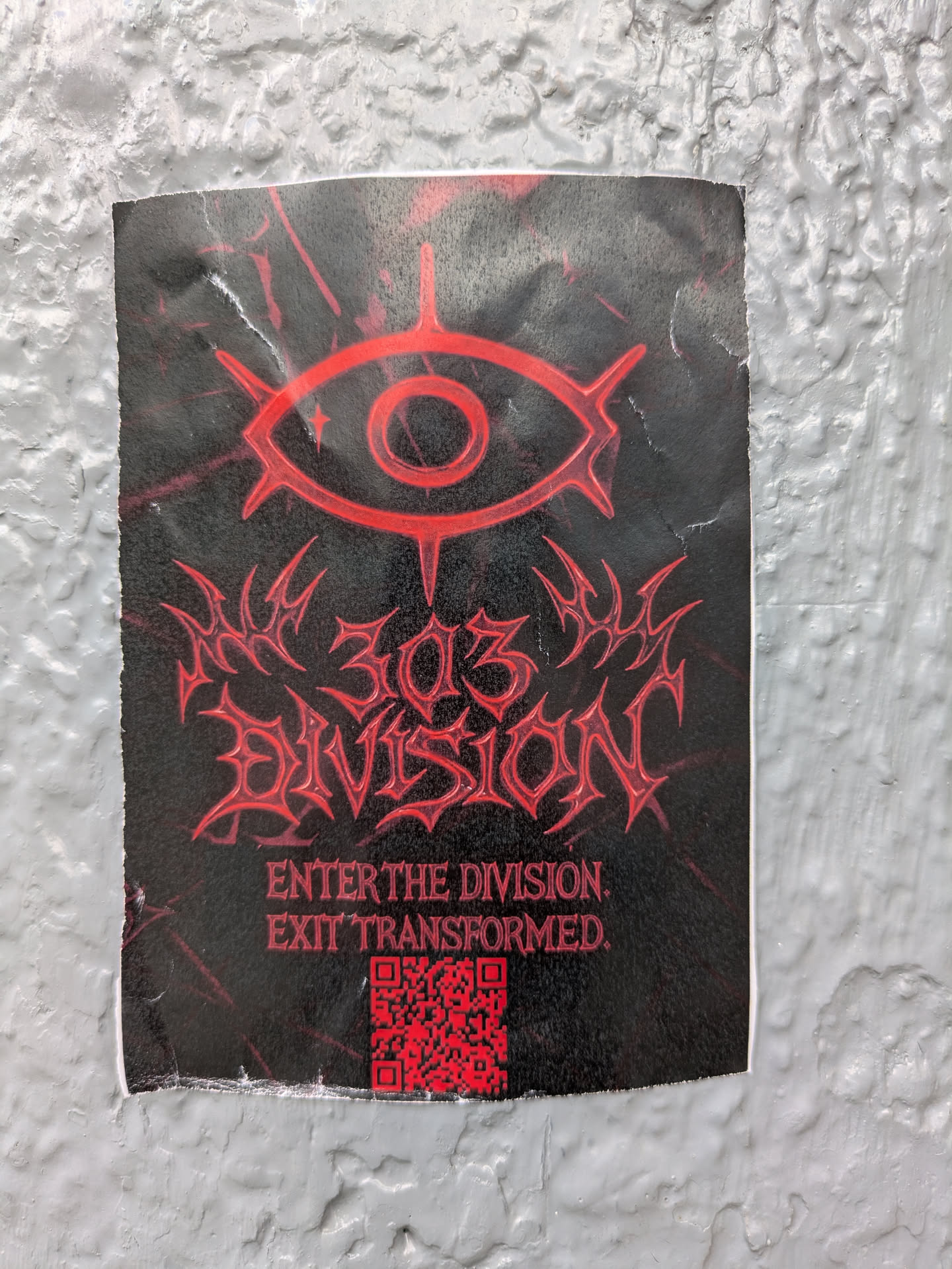 A black sticker with red design featuring an eye symbol, the text '303 DIVISION', and the phrase 'ENTER THE DIVISION. EXIT TRANSFORMED.' There's also a QR code at the bottom.