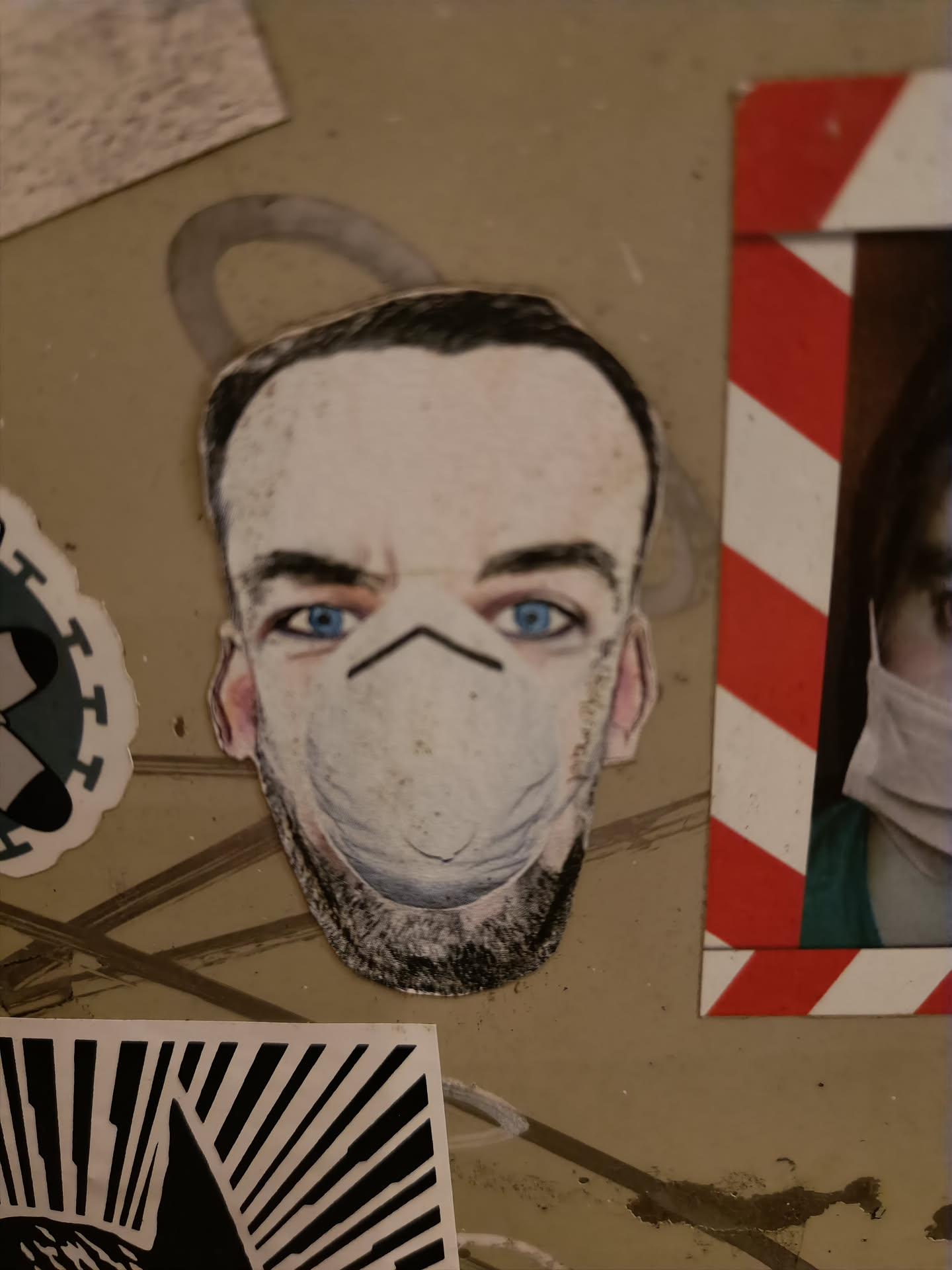 A sticker depicting a man with blue eyes wearing a white N95 facemask. The style is reminiscent of a caricature or a stylized portrait.