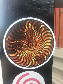 Round sticker with a hypnotic spiral design in fiery orange and black. The center of the spiral has the words "THE END" written in a circle.