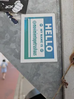 The sticker features a light blue to green gradient and is placed on a metallic surface. It reads "Hello My Name Is" with the name "movimientopetrushaus" written on the left side. The sticker is designed in a gradient color scheme.