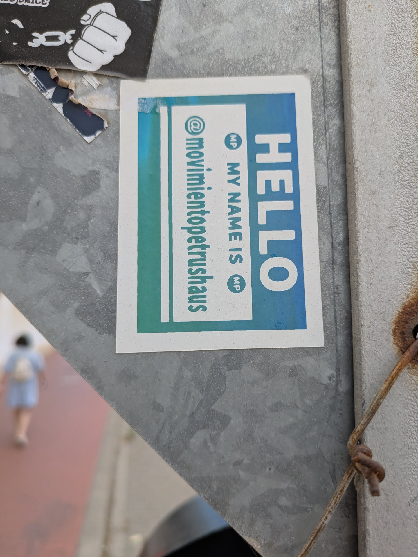 The sticker features a light blue to green gradient and is placed on a metallic surface. It reads "Hello My Name Is" with the name "movimientopetrushaus" written on the left side. The sticker is designed in a gradient color scheme.