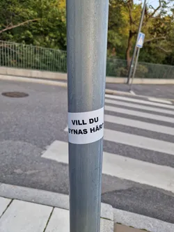 A sticker on a pole at a crosswalk, asking "Do you want to be seen here?" in Swedish.