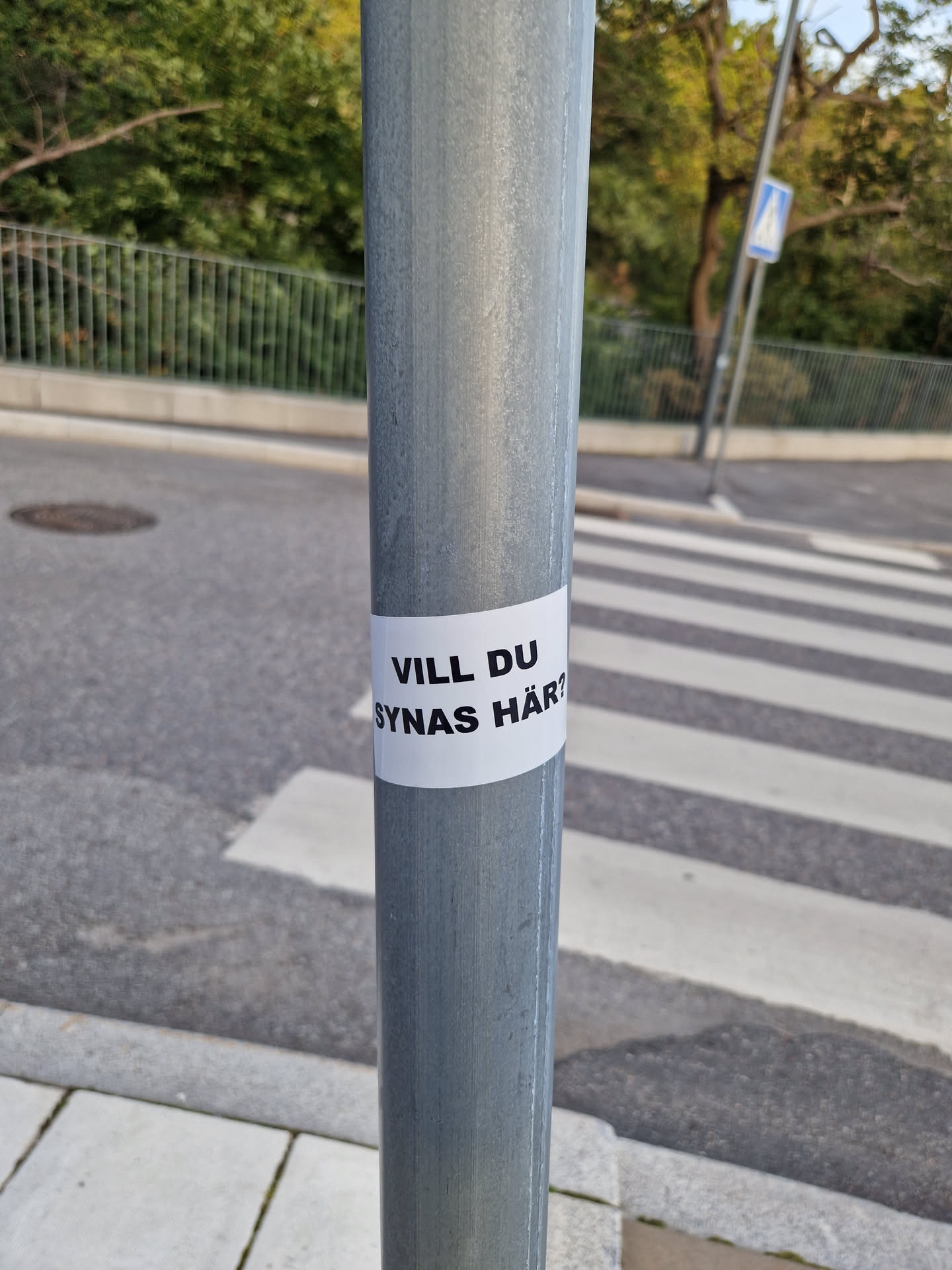 A sticker on a pole at a crosswalk, asking "Do you want to be seen here?" in Swedish.