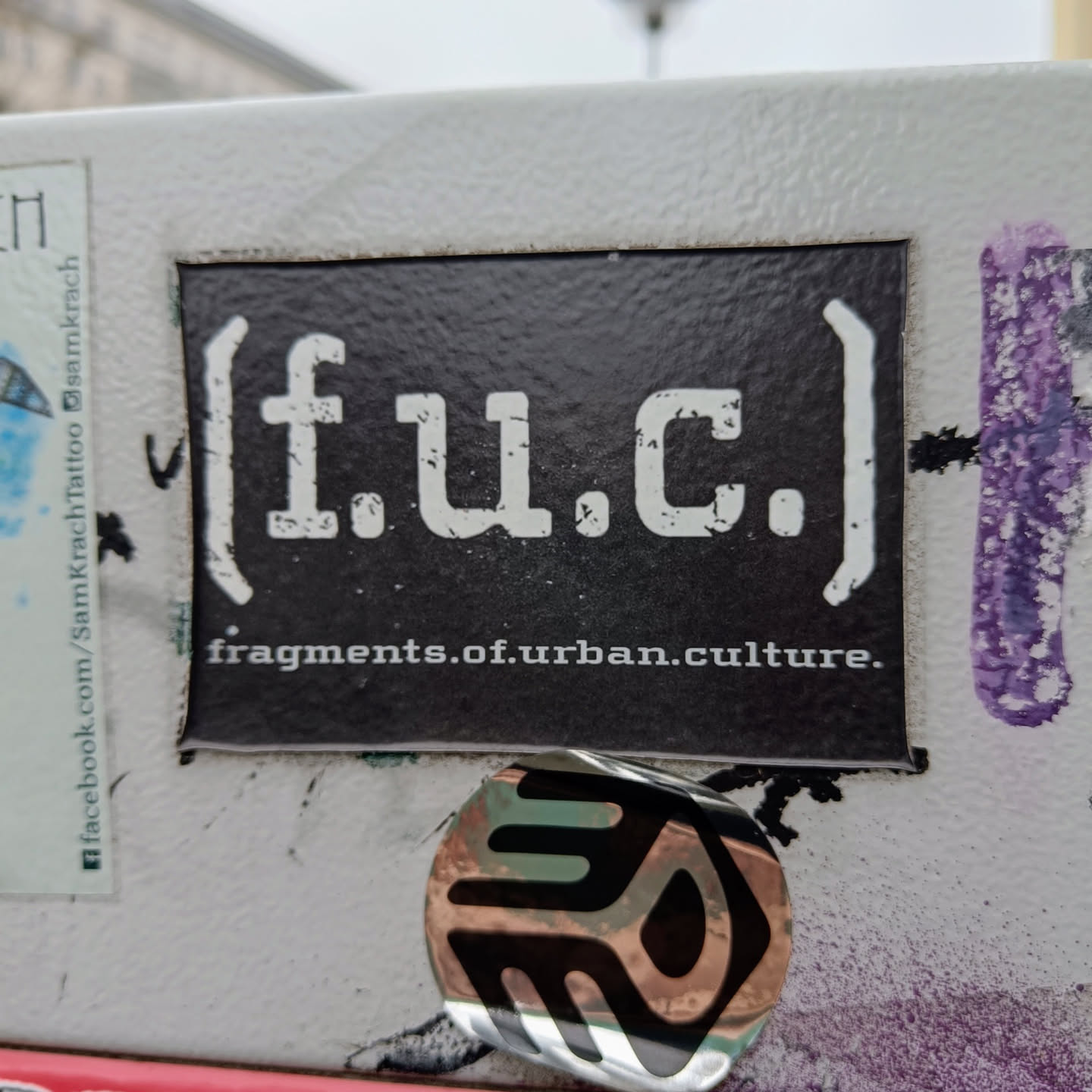 Black and white sticker with the text [f.u.c.] fragments.of.urban.culture. The text is stylized and has a grunge effect.