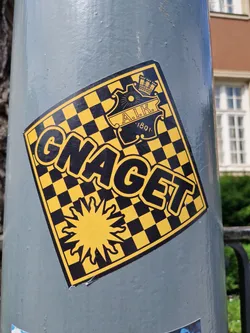 Yellow and black checkered sticker with the word Gnagget and the AIK Solna logo. The sticker has a sunburst design at the bottom.