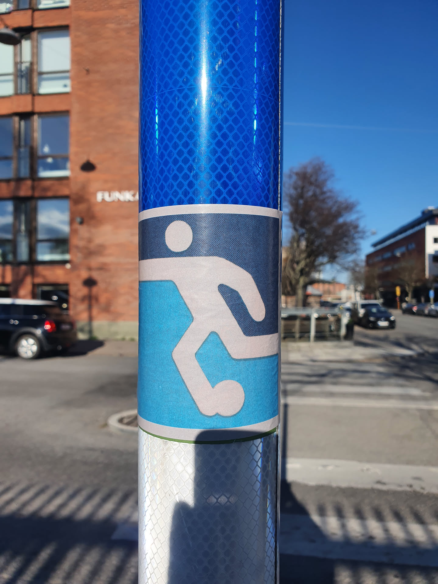 The sticker shows a pictogram of a person kicking a ball.  It's a simple design, likely indicating a nearby soccer field or related activity. The sticker is affixed to a blue reflective post.