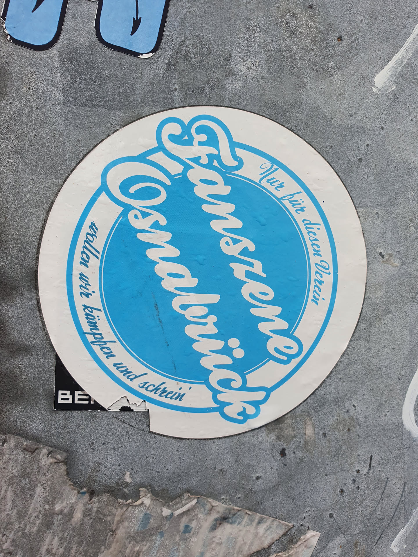 A sticker featuring the text "Fanszene Cosmaulbrück" in a stylized font. The text is written in German and translates to "Fan scene Cosmaulbrück". The sticker is circular with a blue central area and a white outer ring. There is additional text in the outer ring, which appears to be a motto or slogan.