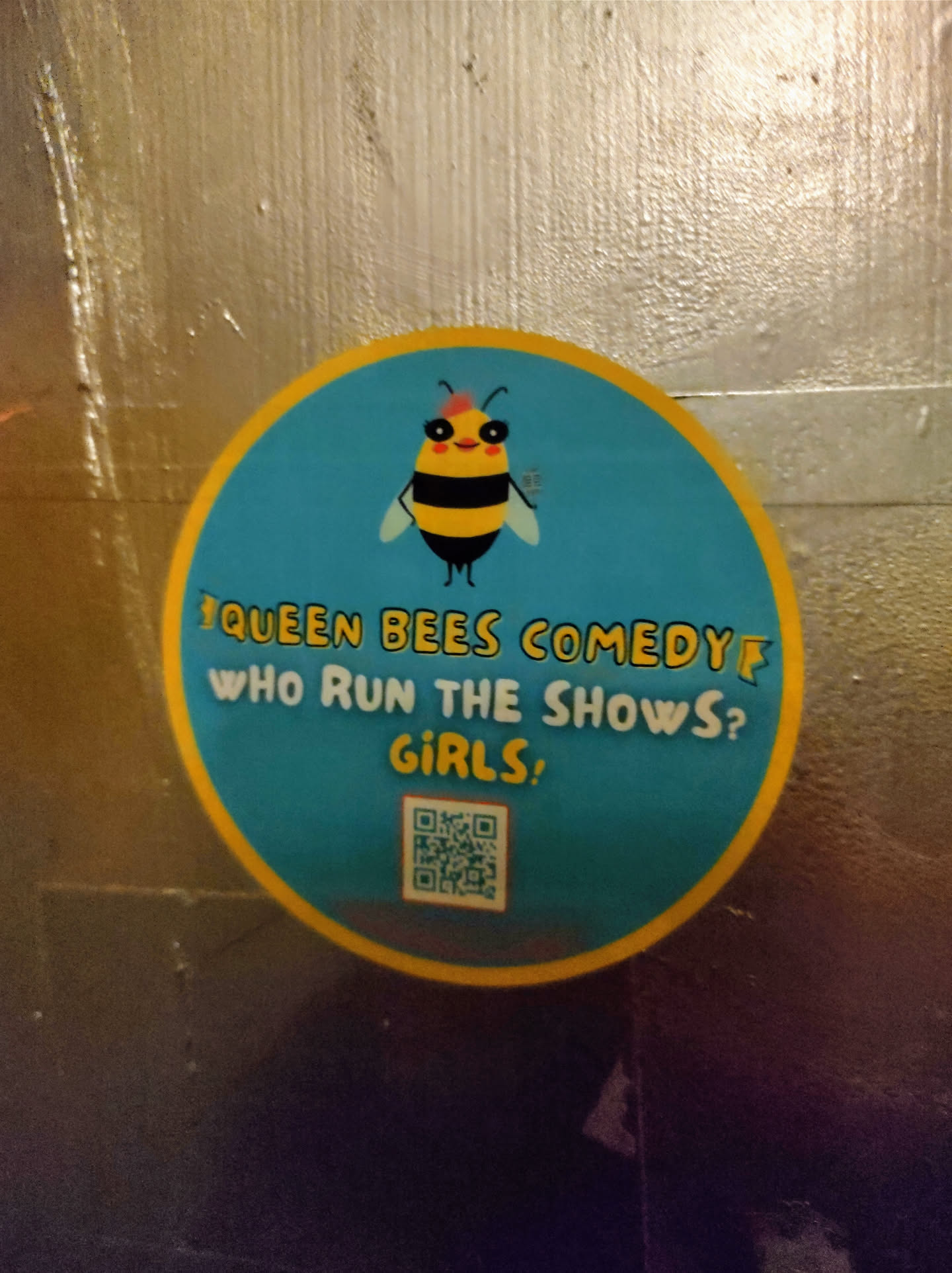Round sticker featuring a cartoon bee and the text "Queen Bees Comedy. Who run the shows? Girls!"  It includes a QR code at the bottom.