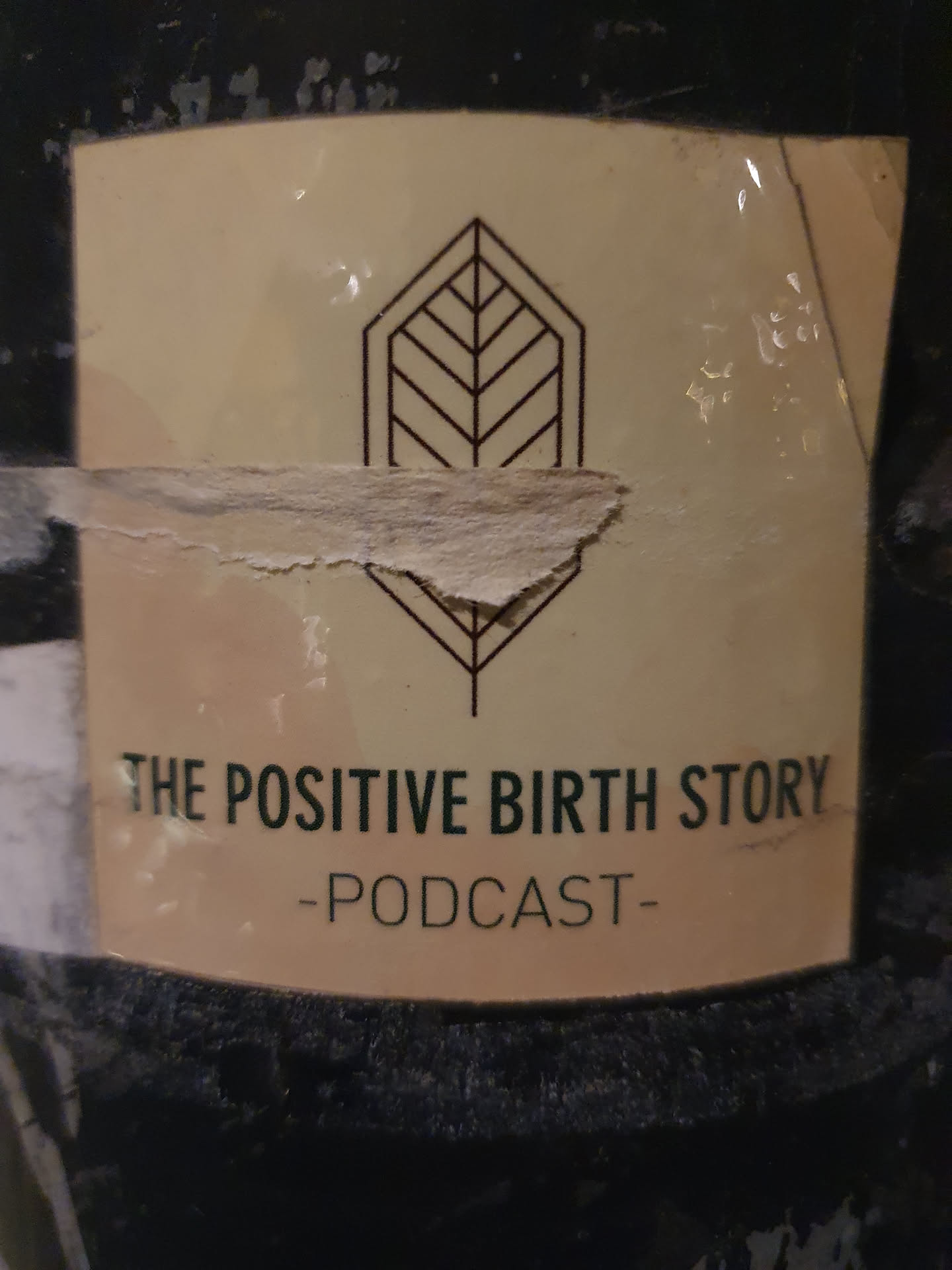 A beige sticker with a minimalist leaf design and the text "THE POSITIVE BIRTH STORY -PODCAST-". The sticker is slightly damaged.