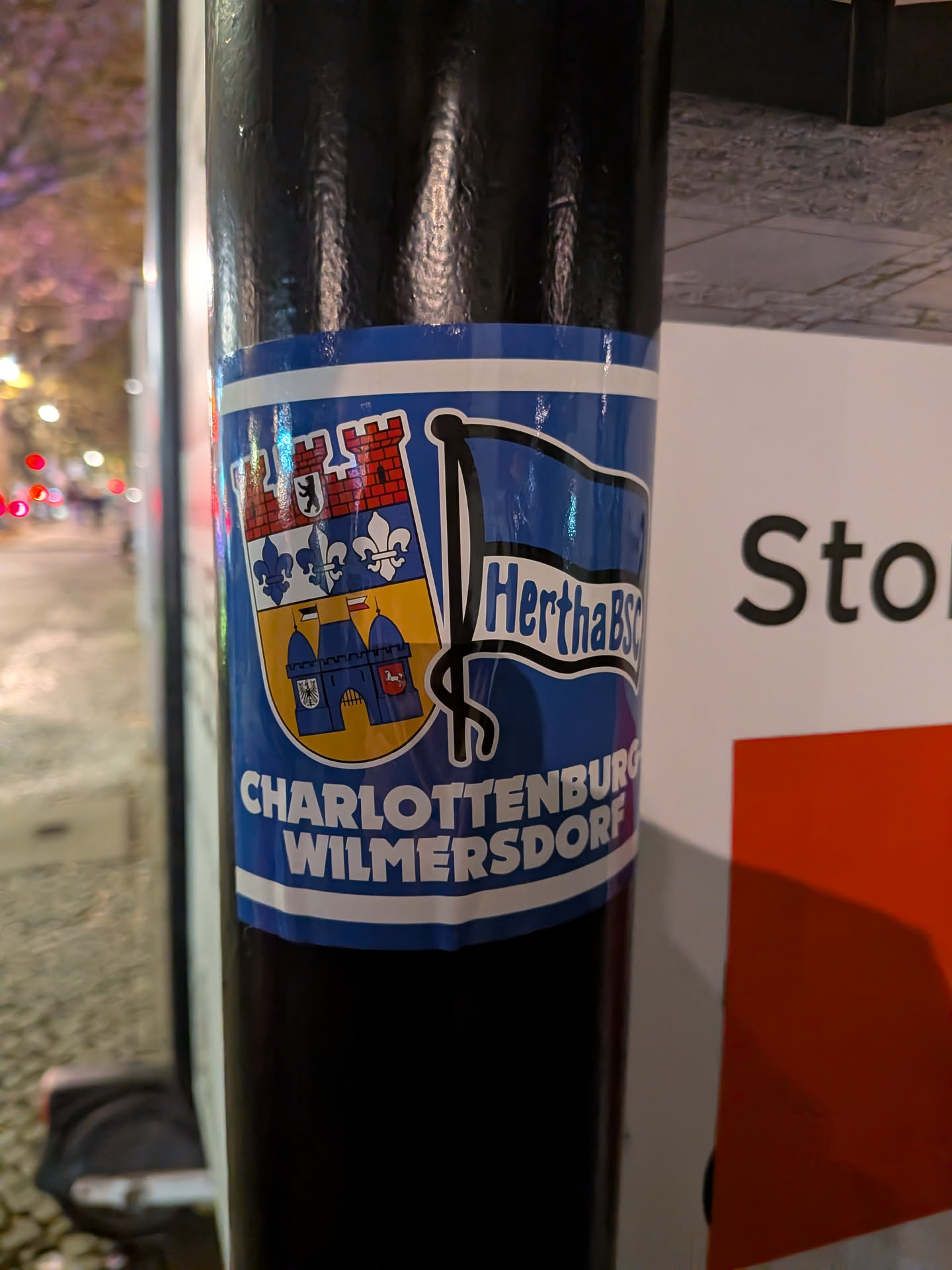 A rectangular blue sticker featuring the coat of arms of the Berlin borough Charlottenburg-Wilmersdorf on the left, and the waving blue-and-white flag logo of Hertha BSC on the right. Below the emblems, the district name 'CHARLOTTENBURG WILMERSDORF' is printed in bold white uppercase lettering, framed by a thin white border around the outer edge.