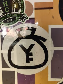 A round sticker featuring a stylized Yen symbol in black on a white background. The sticker shows some wear and tear.