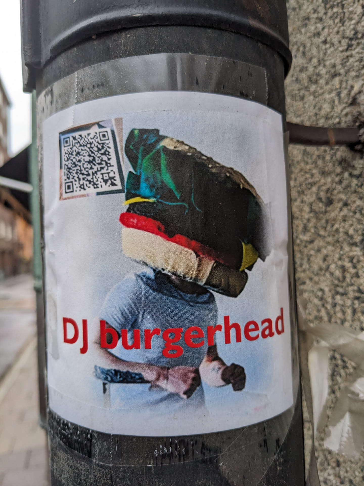 Sticker featuring an illustration of a person with a burger-shaped head, styled as a DJ.  A QR code is present in the top left corner. The style is colorful and slightly surreal.
