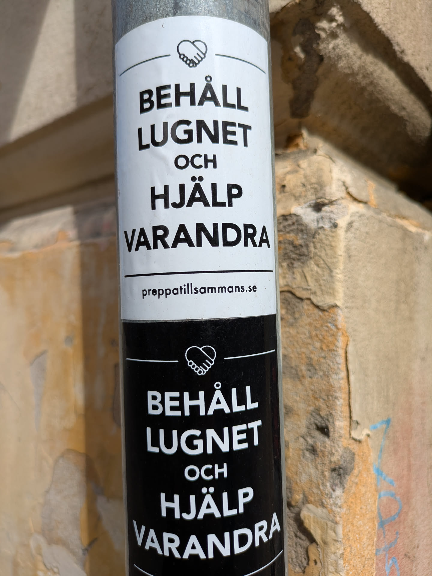 The sticker features the text "BEHÅLL LUGNET OCH HJÄLP VARANDRA" which translates to "KEEP CALM AND HELP EACH OTHER" in Swedish. There is a website url at the bottom of the sticker. The top sticker is white and the bottom is black.