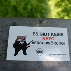 A sticker featuring a Shiba Inu in a suit holding a gun, with text in German stating "There is no NATO conspiracy!" and a Twitter hashtag #WeAreNATO.  The sticker also includes a logo that appears to be related to German news.