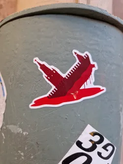 A sticker depicting a minimalist illustration of the Kremlin towers submerged or bleeding in a pool of red, possibly symbolizing conflict or political turmoil.  The style is simple and graphic.